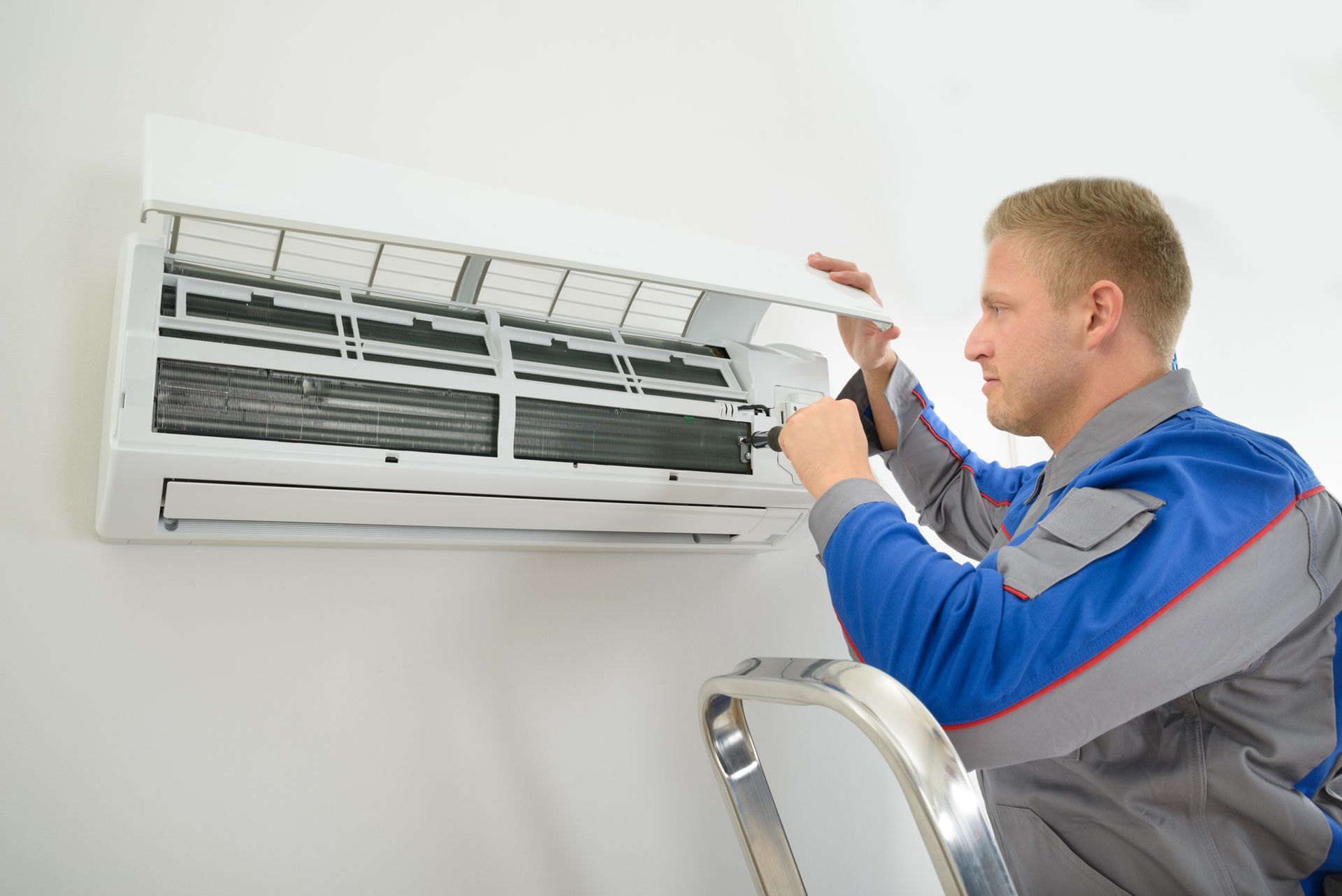 A man is working on an air conditioner on a ladder.
