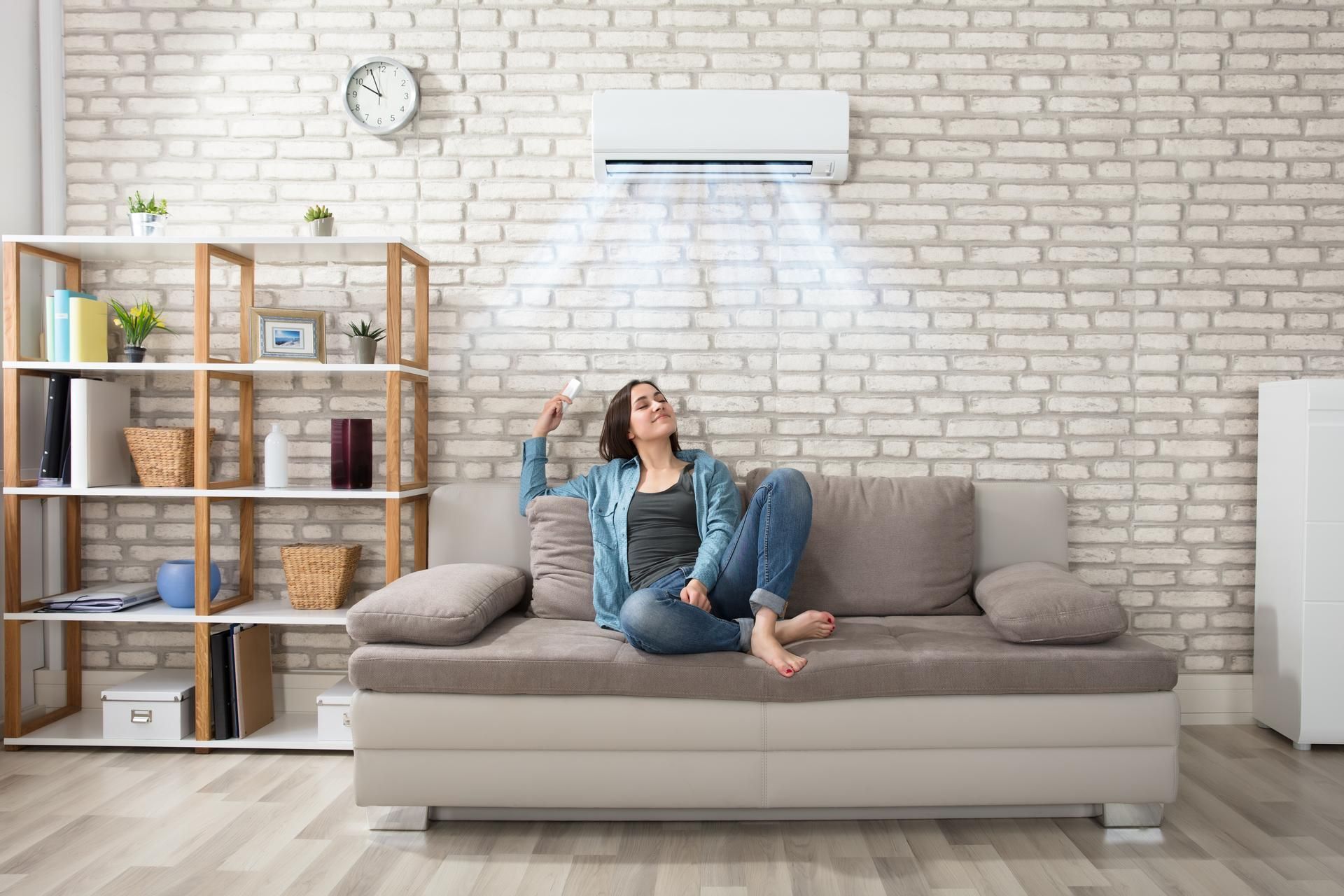 A woman is sitting on a couch under an air conditioner in a living room.