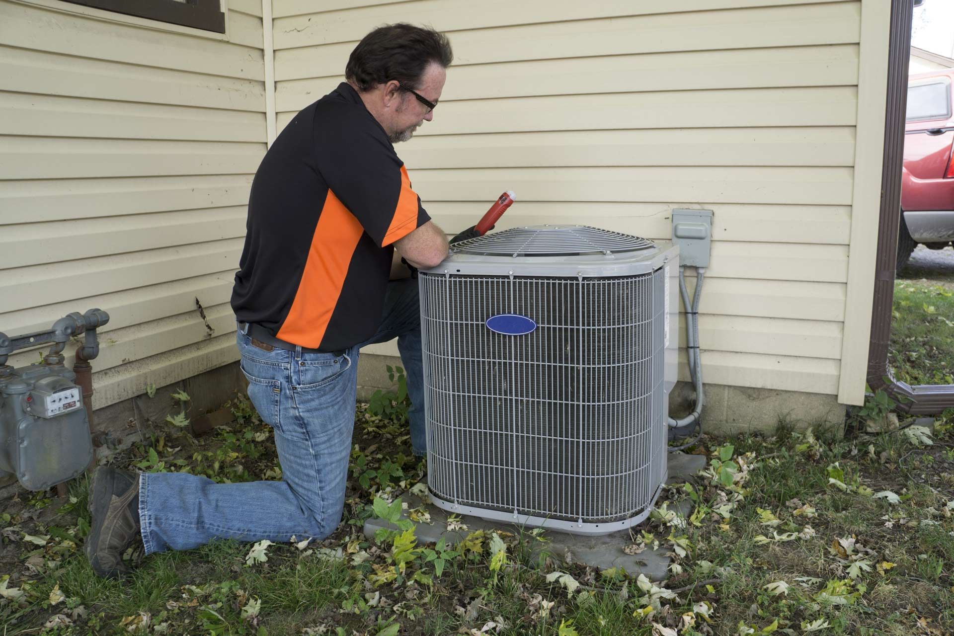 A man is working on an air conditioner outside of a house.