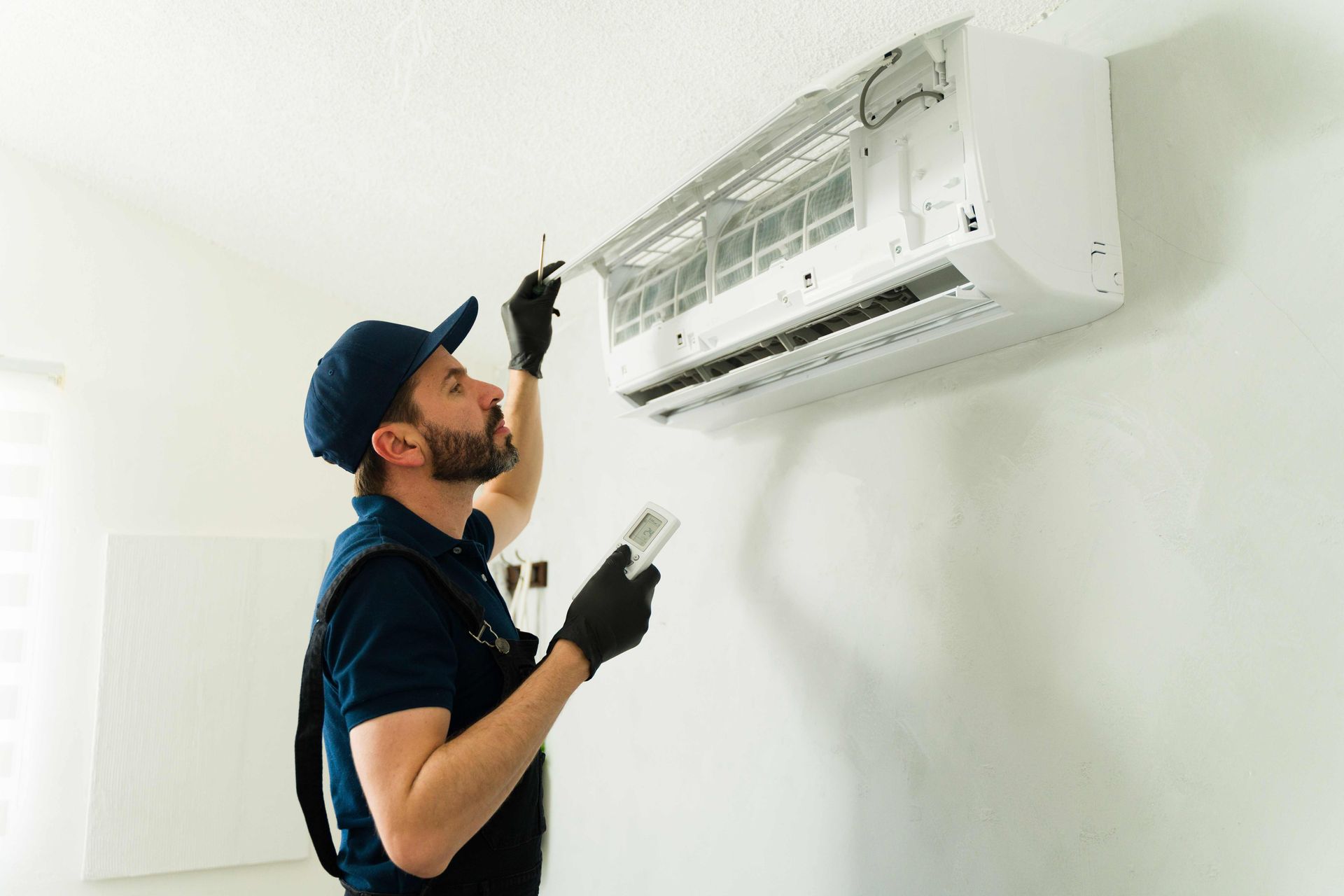 Technician inspecting a wall-mounted air conditioner with tools in a white room