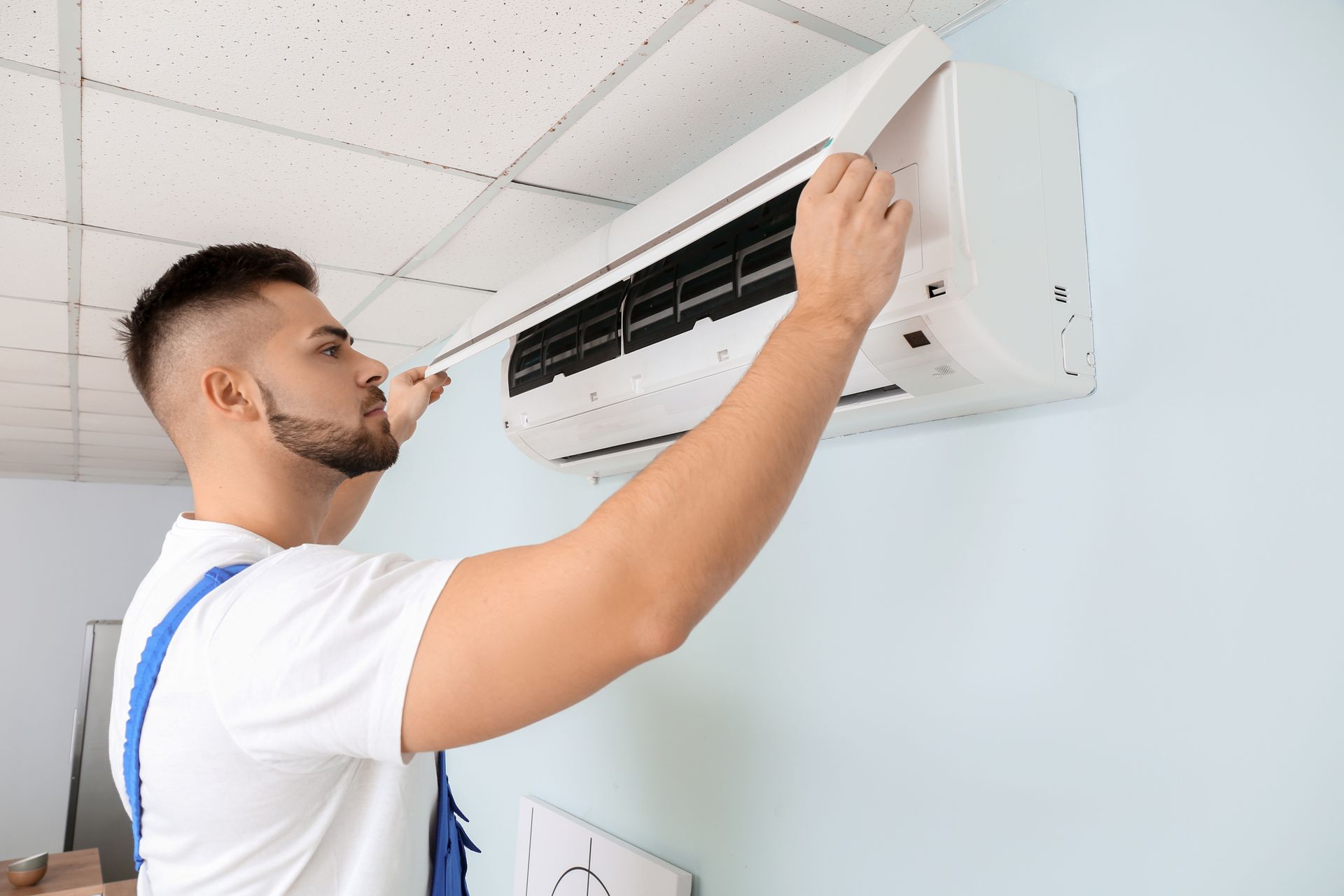 Male technician repairing air conditioner indoors.