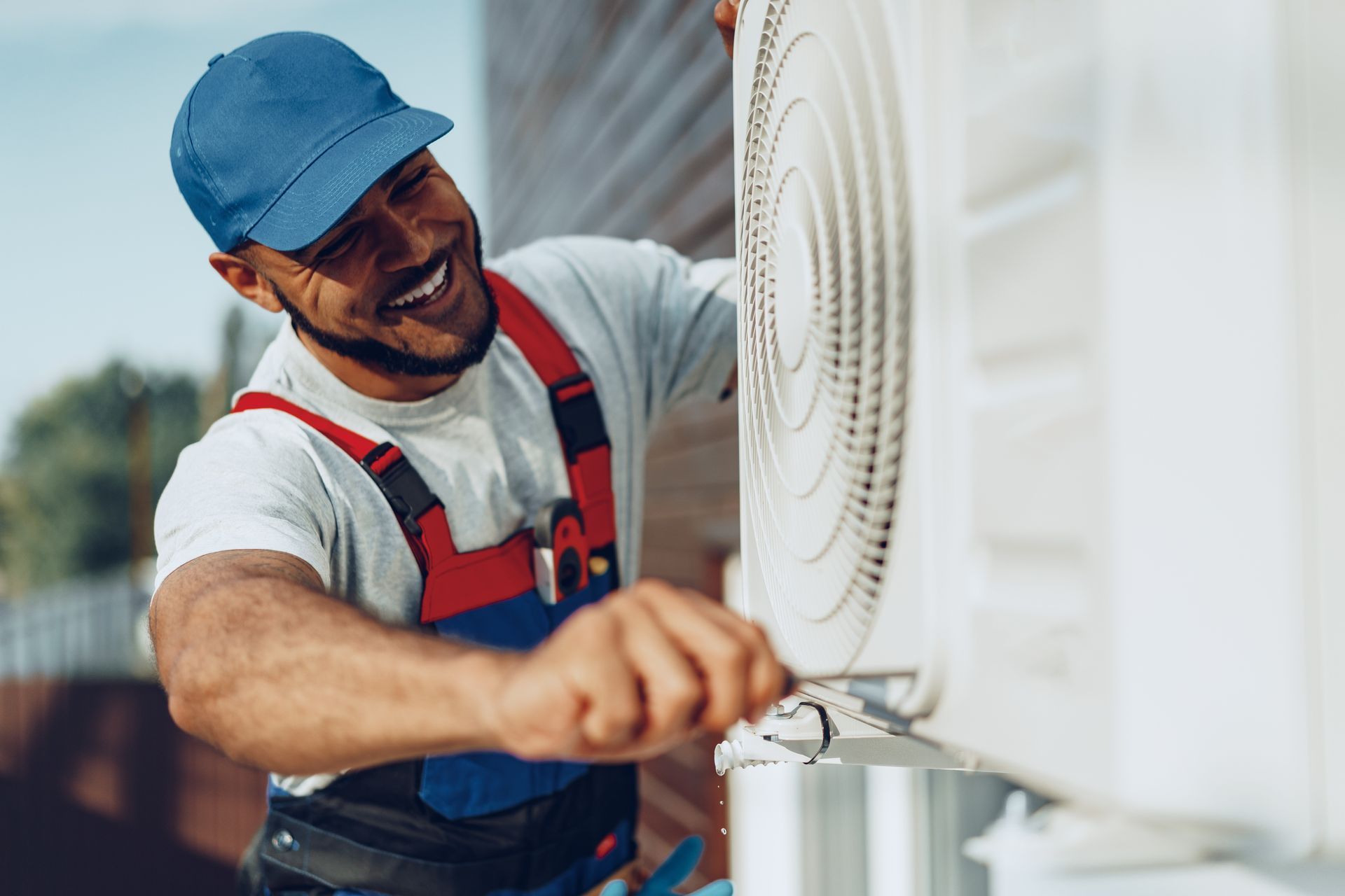 Technician adjusting an outdoor air conditioning unit with a screwdriver.
