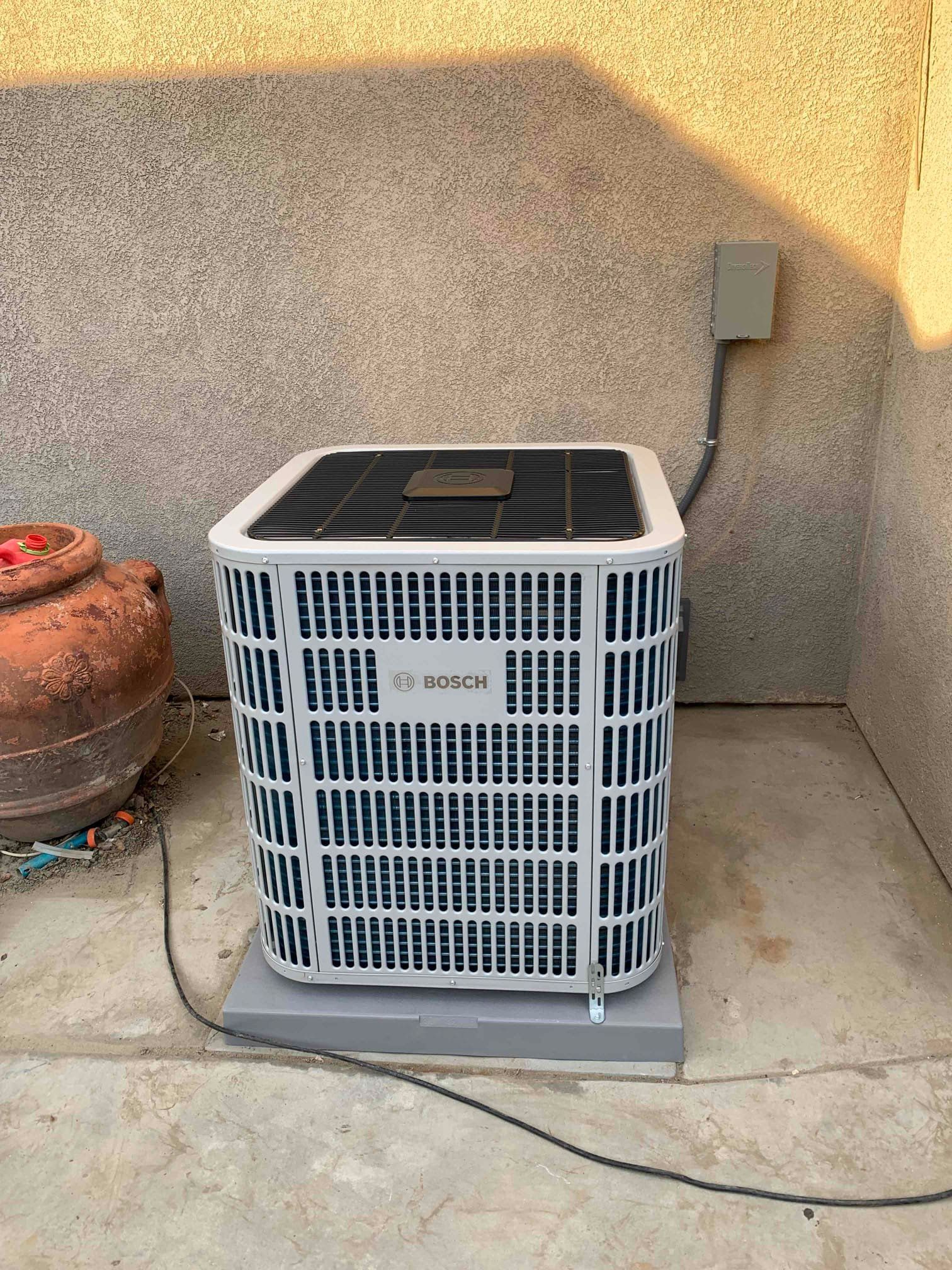 Air conditioning unit, white and blue, on a concrete pad against a wall. Electrical box nearby.
