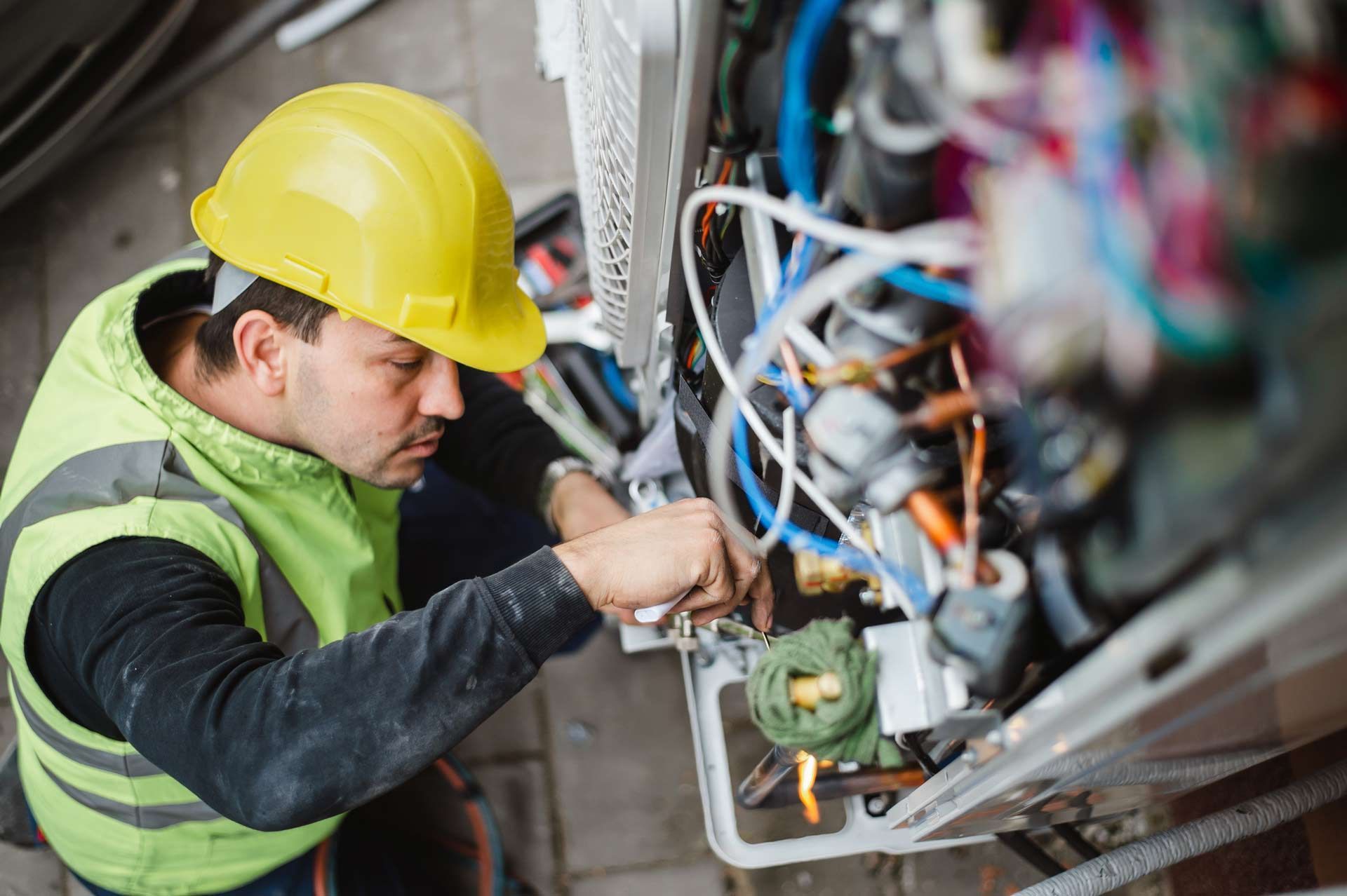 A man wearing a hard hat and safety vest is working on a machine.