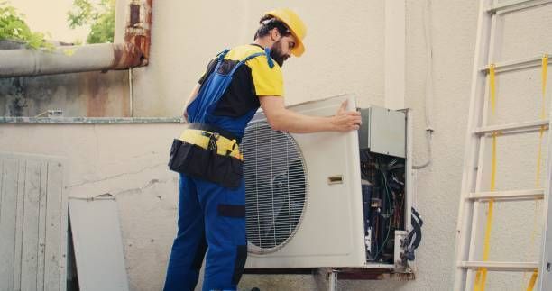 A HVAC contractor with protection gear is fixing a HVAC unit outside a building.
