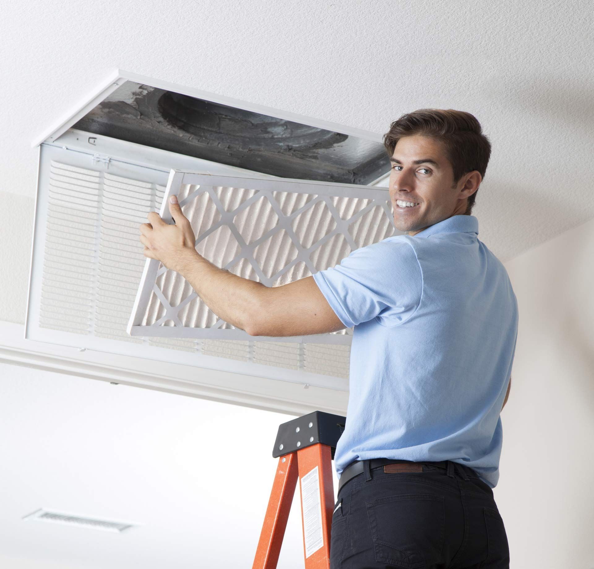 A man is standing on a ladder fixing an air vent