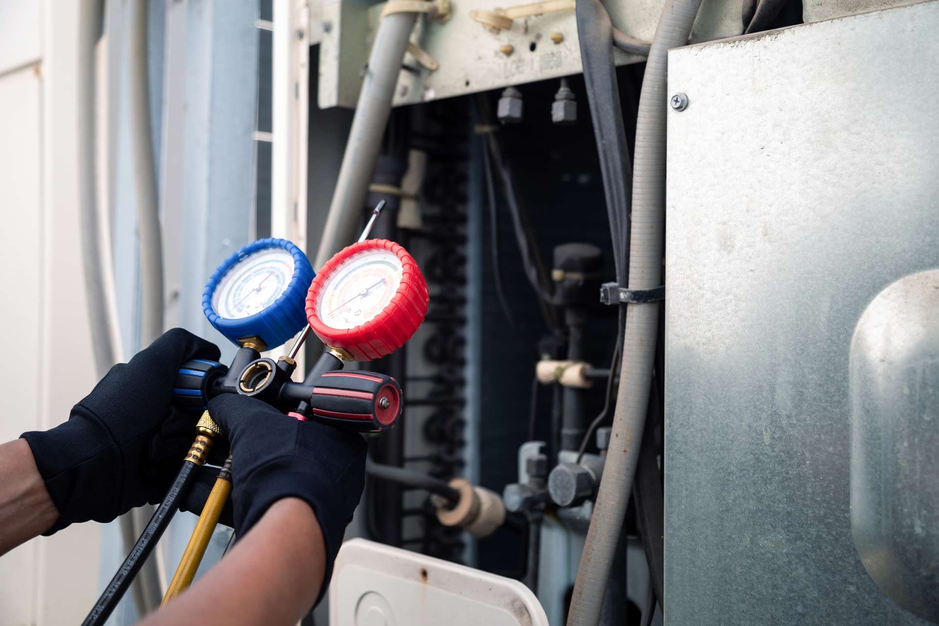 A person is working on an air conditioner with two gauges.