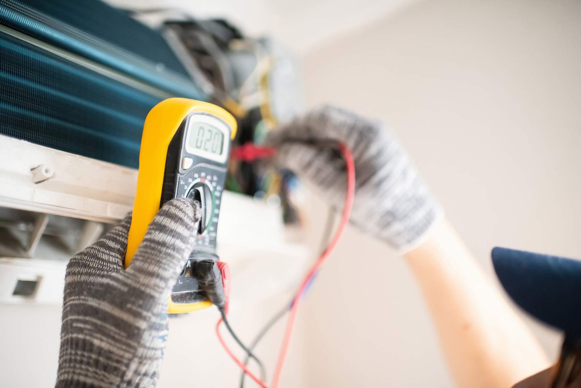 Technician with multimeter repairing air conditioner at home.