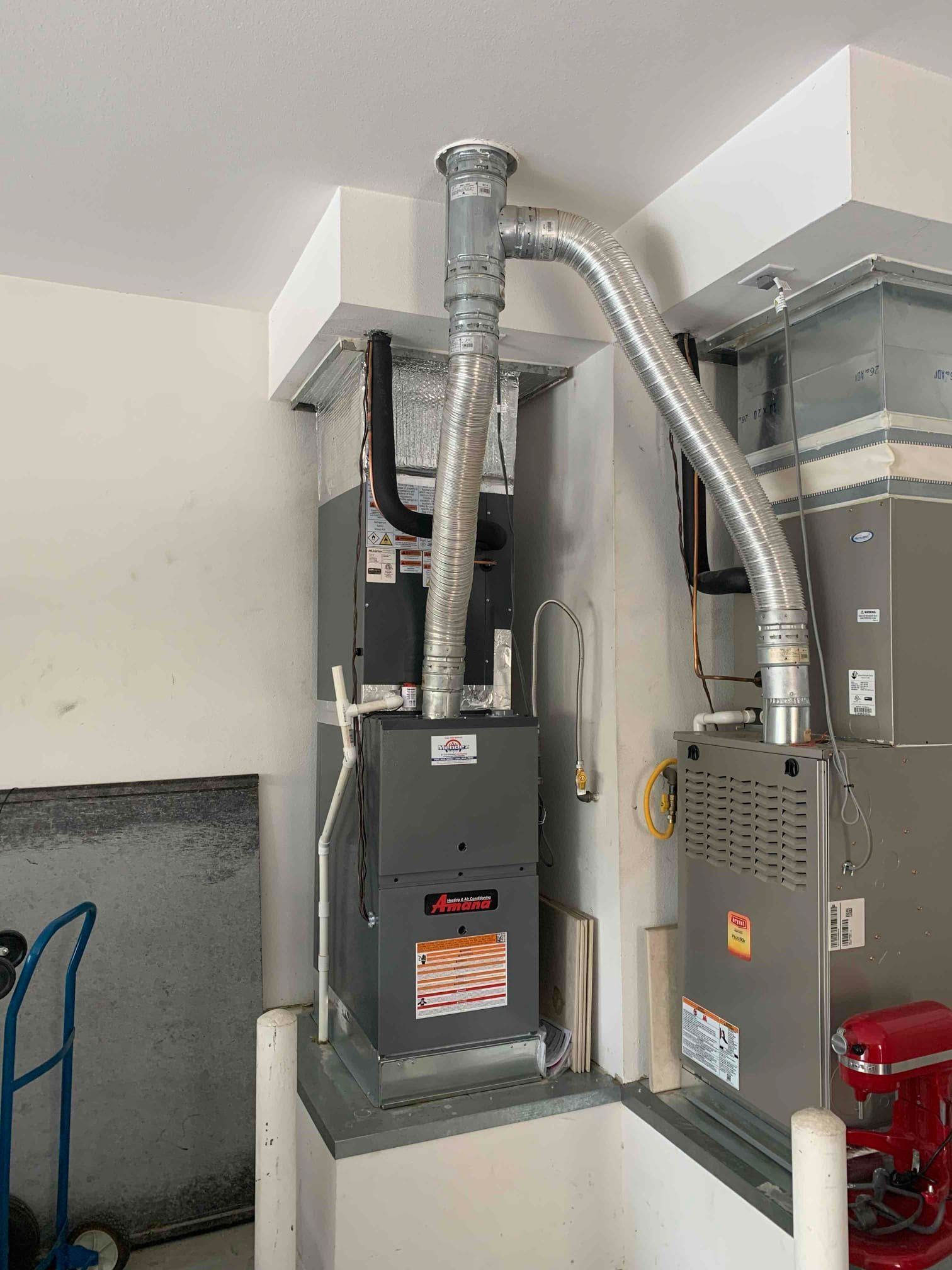 Furnace and air handler units installed in a utility area with ductwork and vent.