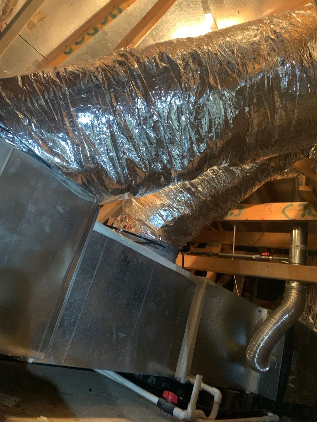 HVAC ductwork in an attic, with metallic flex ducting and rigid metal ducting. Wooden beams are visible.