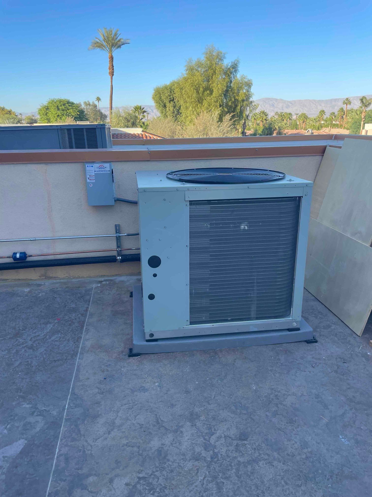 HVAC unit on a flat rooftop against a blue sky with a palm tree.