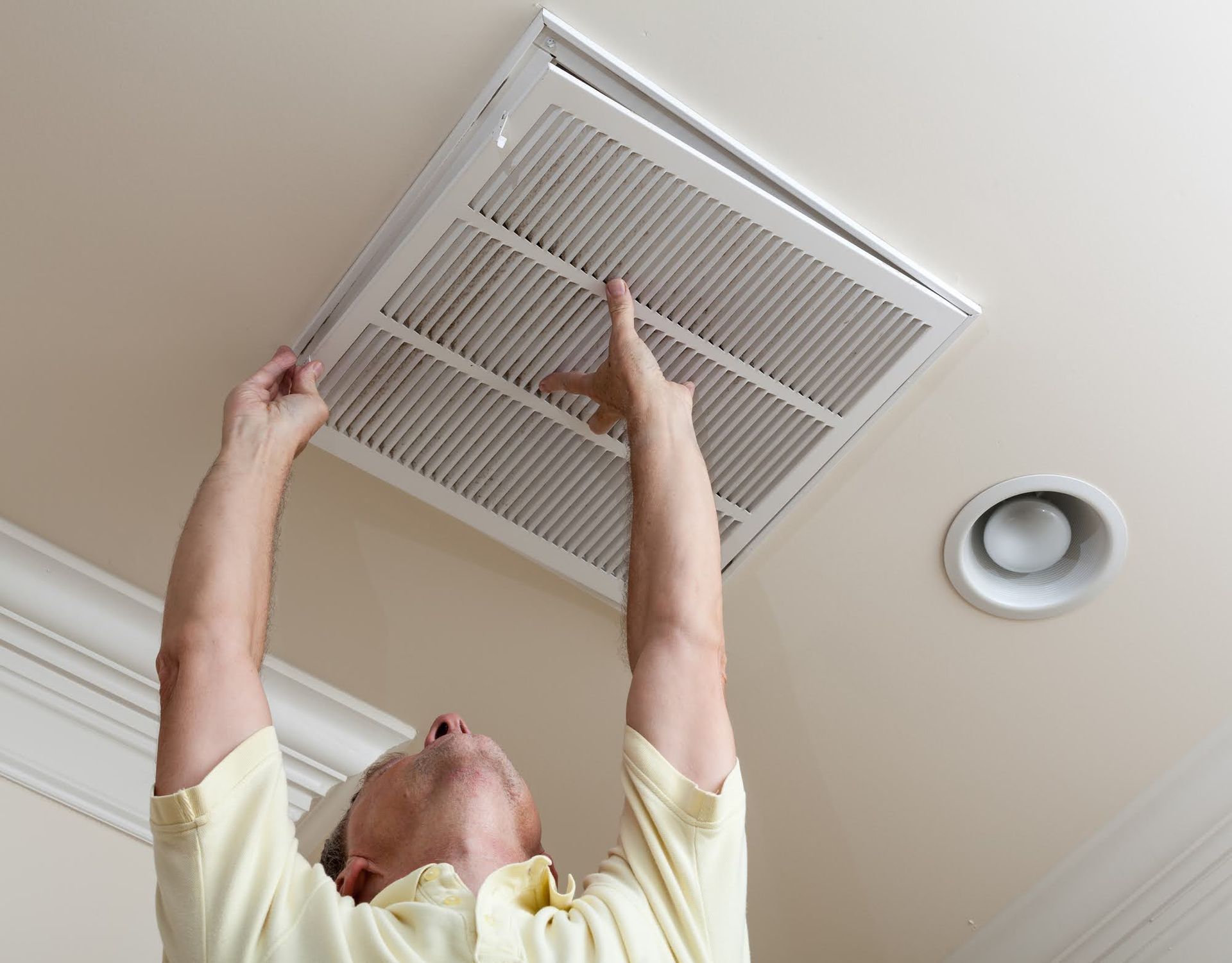 A man is looking up at a vent on the ceiling.