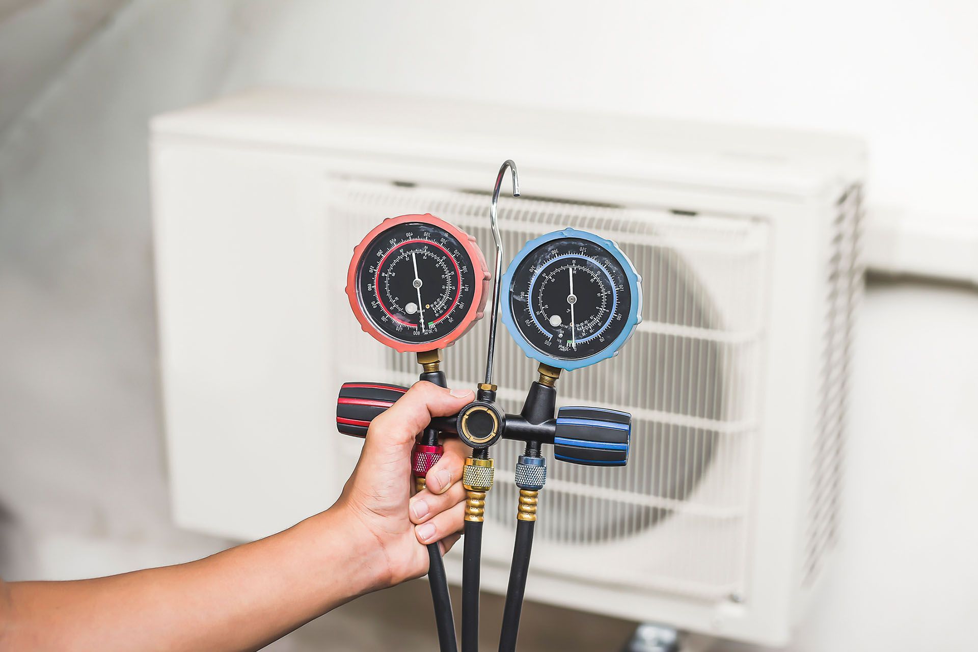 Technician using HVAC manifold gauges to test air conditioner pressure during maintenance service.