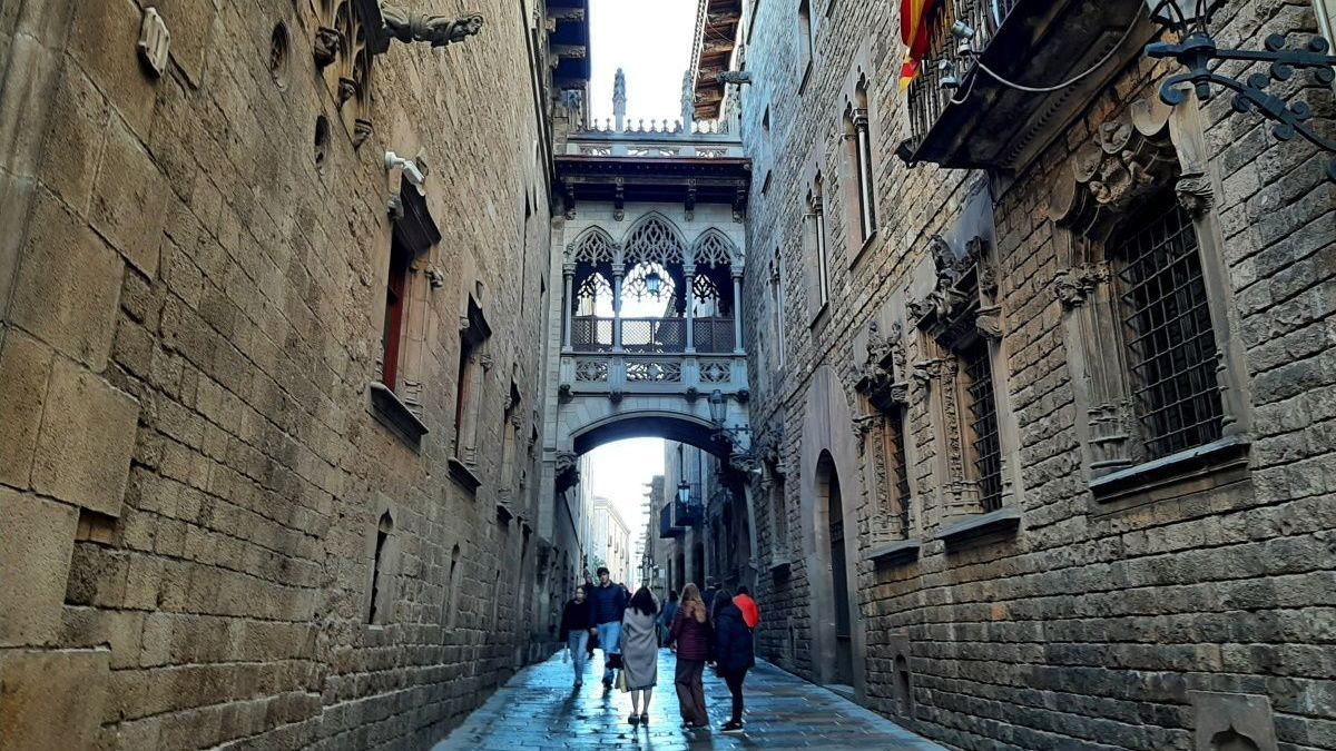 Barcelona A group of people are walking down a narrow street between two brick buildings
