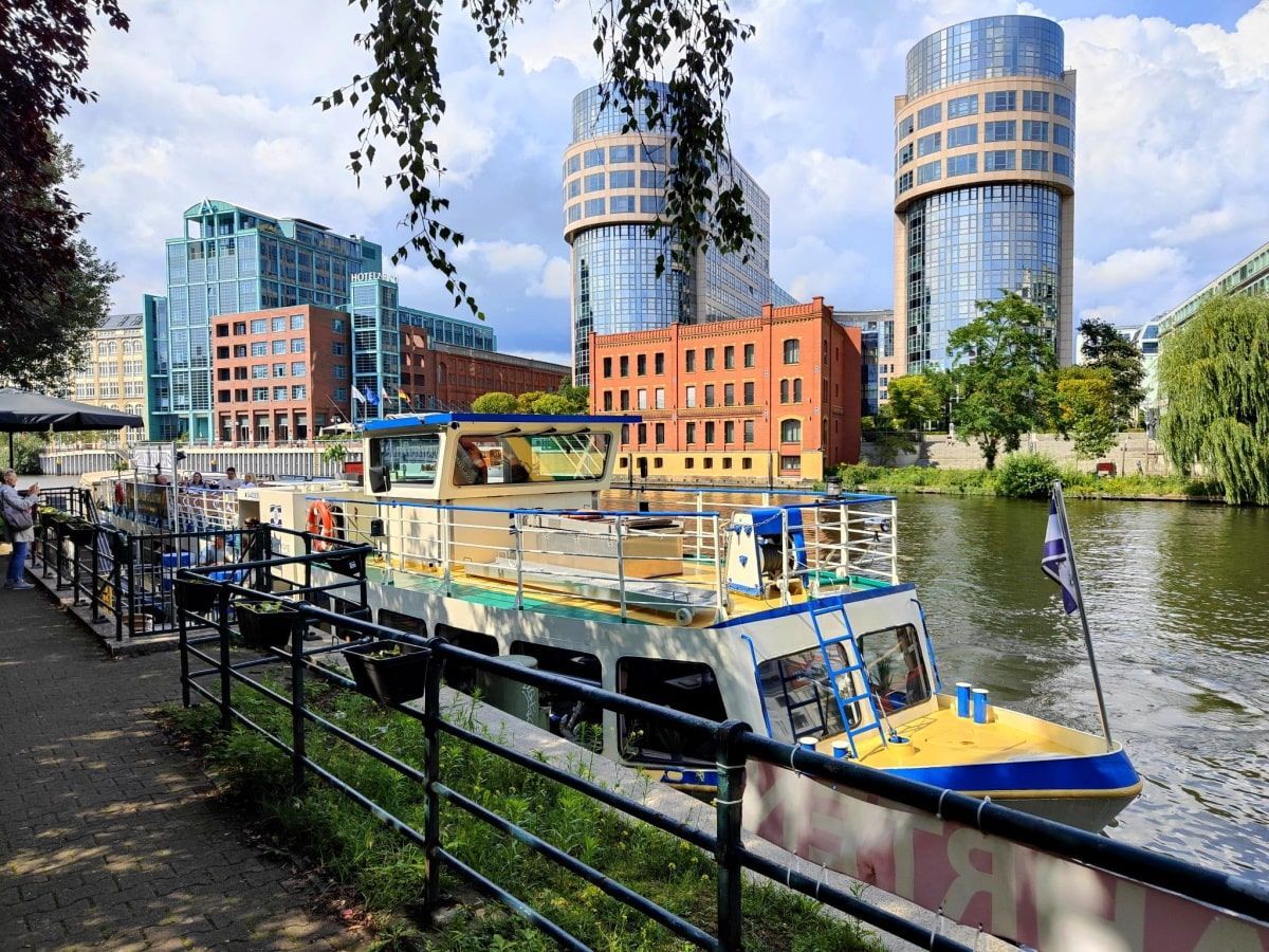 Berlin Cityschiffsfahrt: A boat docked by a walkway on a canal with buildings in the background.