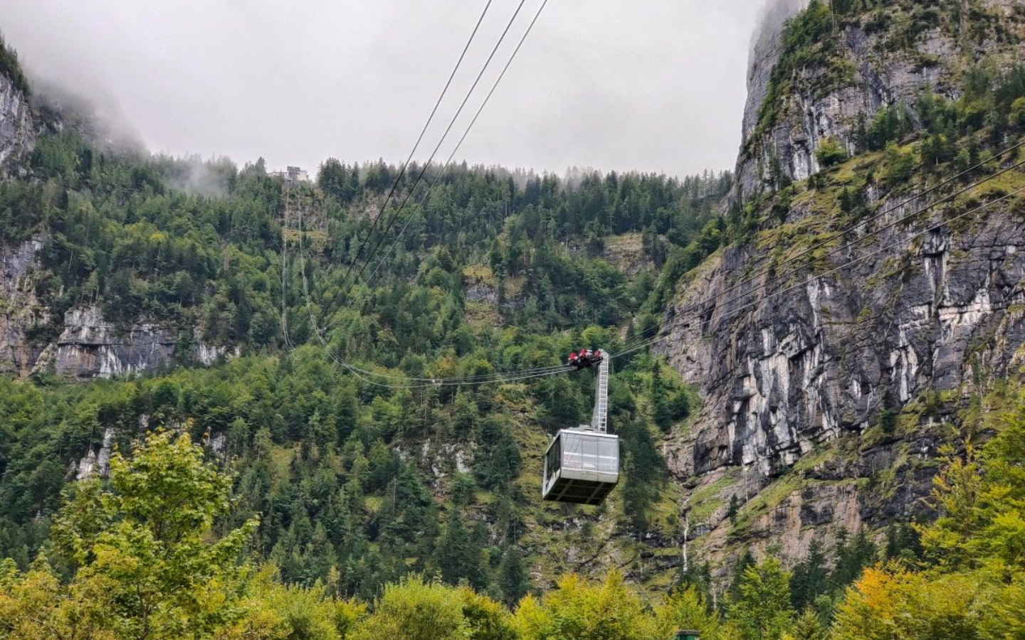 Bergbahn Dachstein Krippenstein Cable car ascending a lush green mountain, with a cloudy sky.