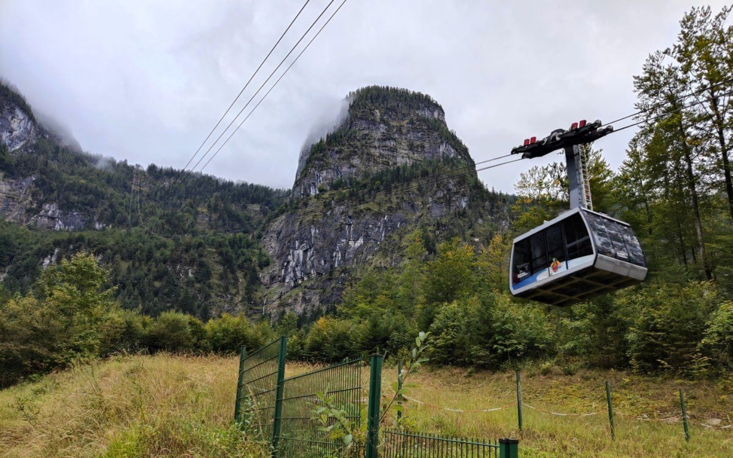 Bergbahn Cable car ascending a mountain, with a dark gray and white cabin and a cloudy sky.
