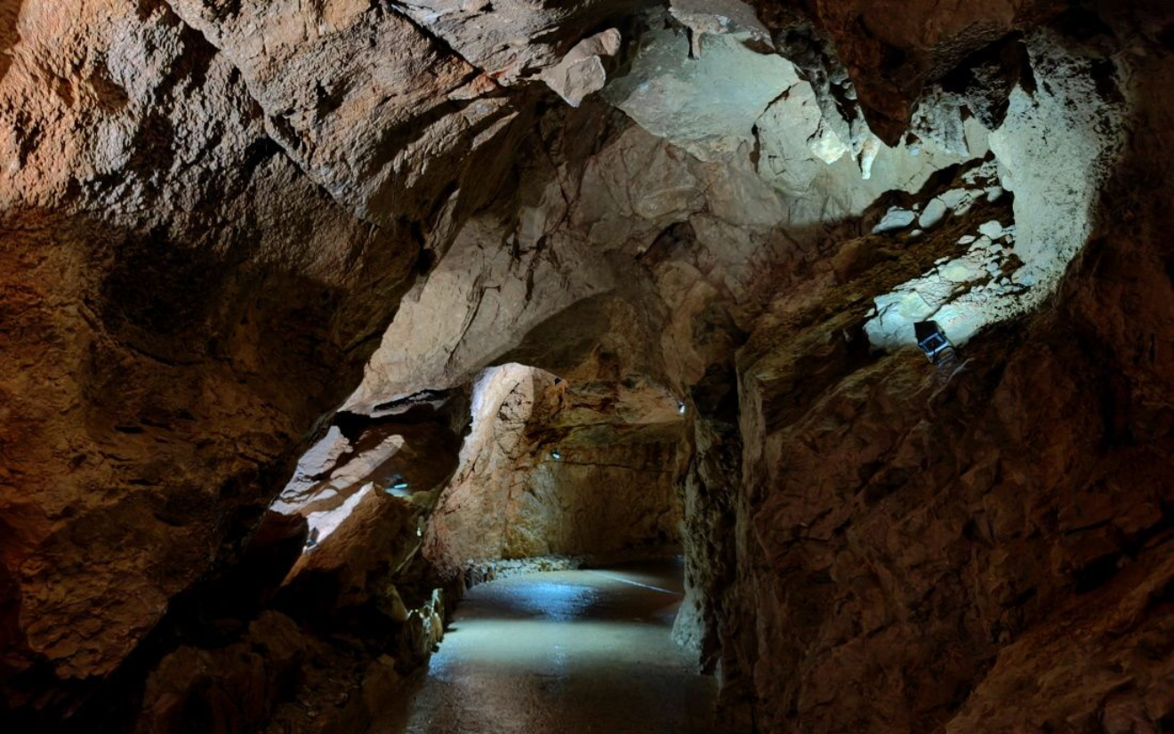 Rieseneishöhle Cave interior with pathway, wet ground, and rough rock walls. Soft lighting illuminates the path.