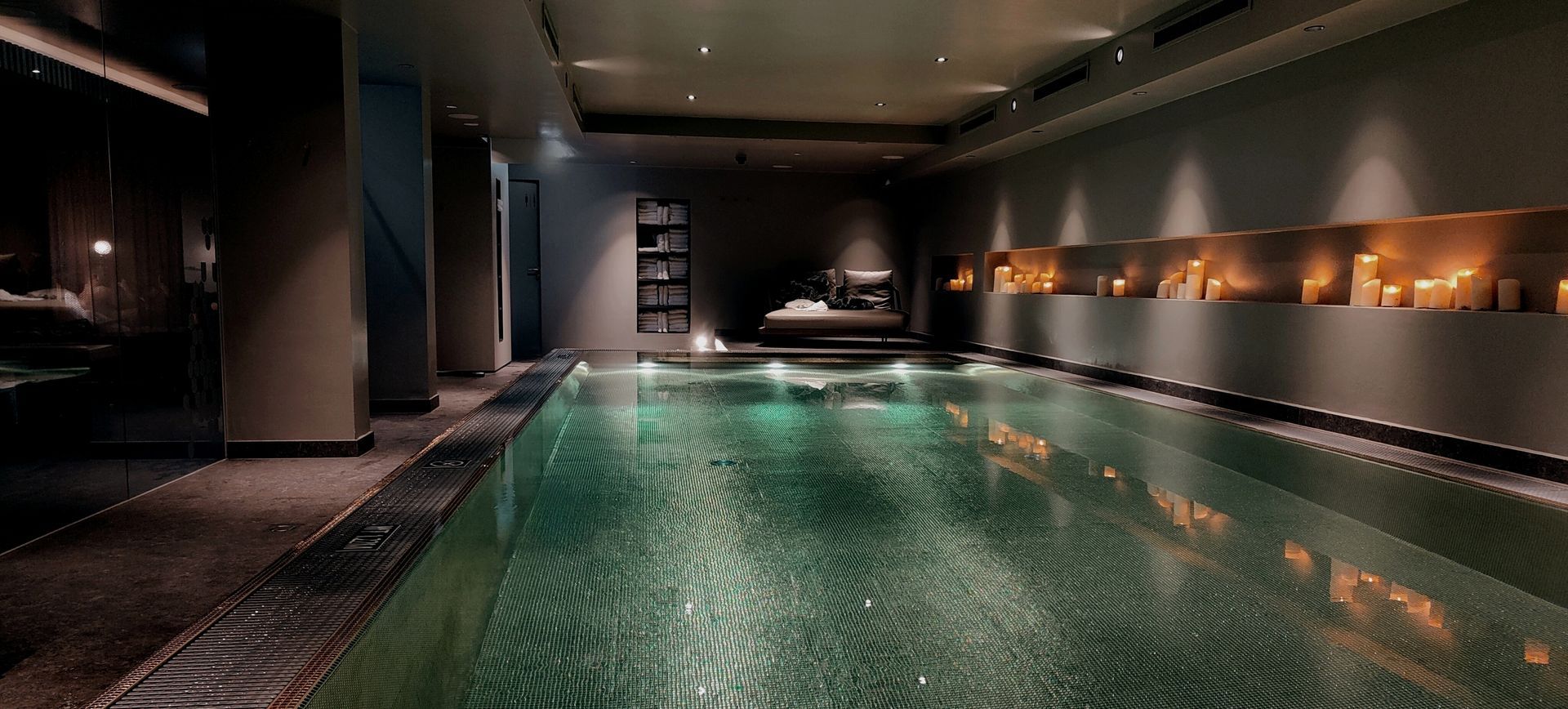 Indoor spa with green-tiled pool, dark walls, ambient lighting, and candles along the wall.