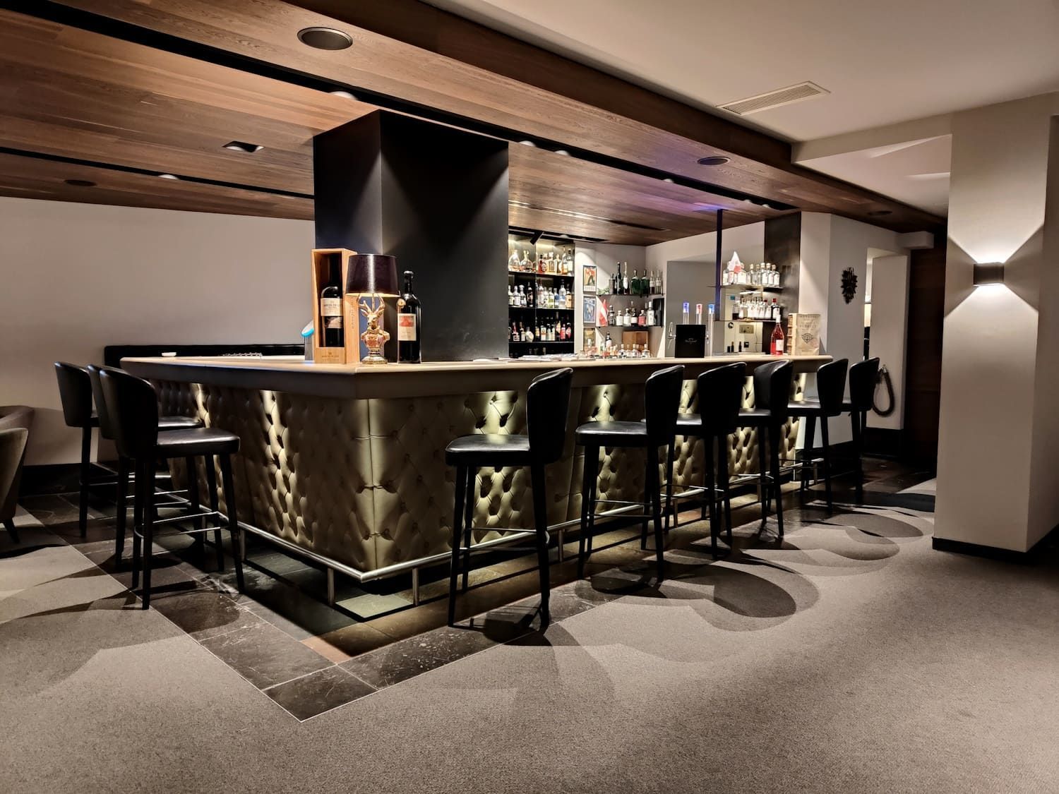 Bar with black stools, illuminated countertop, and liquor bottles against a wood-paneled ceiling.