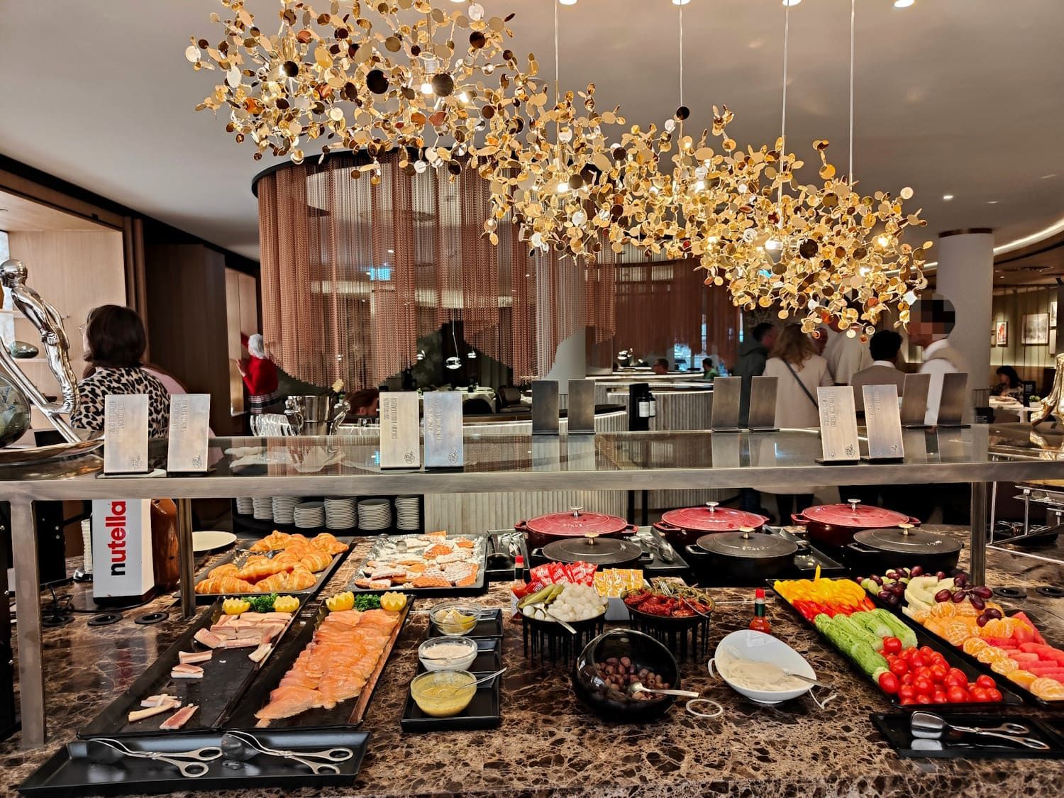 Buffet with various food items on display under ornate lighting fixture.