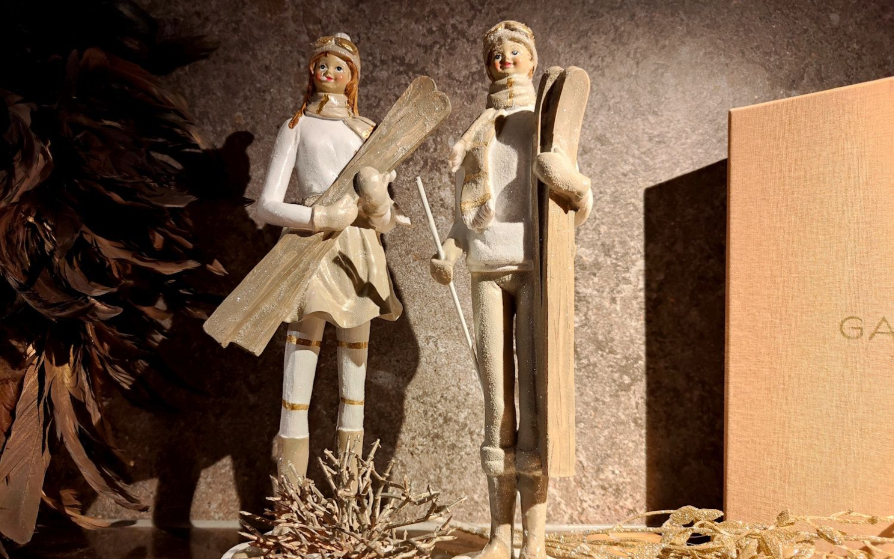 Two decorative figurines stand beside a brown surface, one holding a wooden prop.