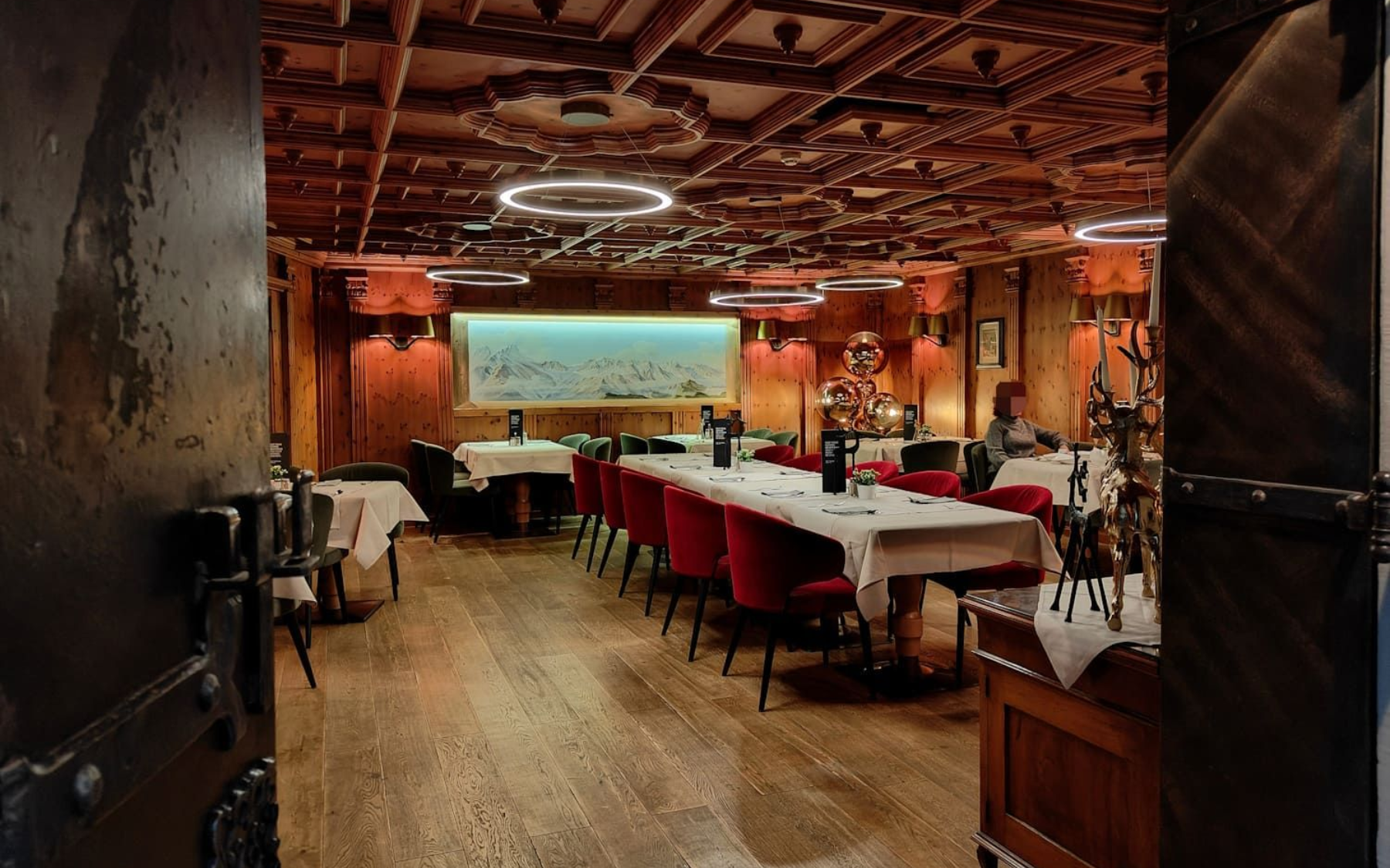 Restaurant interior with wood paneling, tables set with white tablecloths, and red chairs.