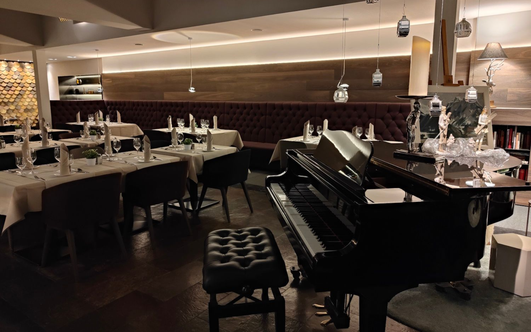Interior of a dimly lit restaurant with tables set for dinner. A grand piano sits near a dining area.