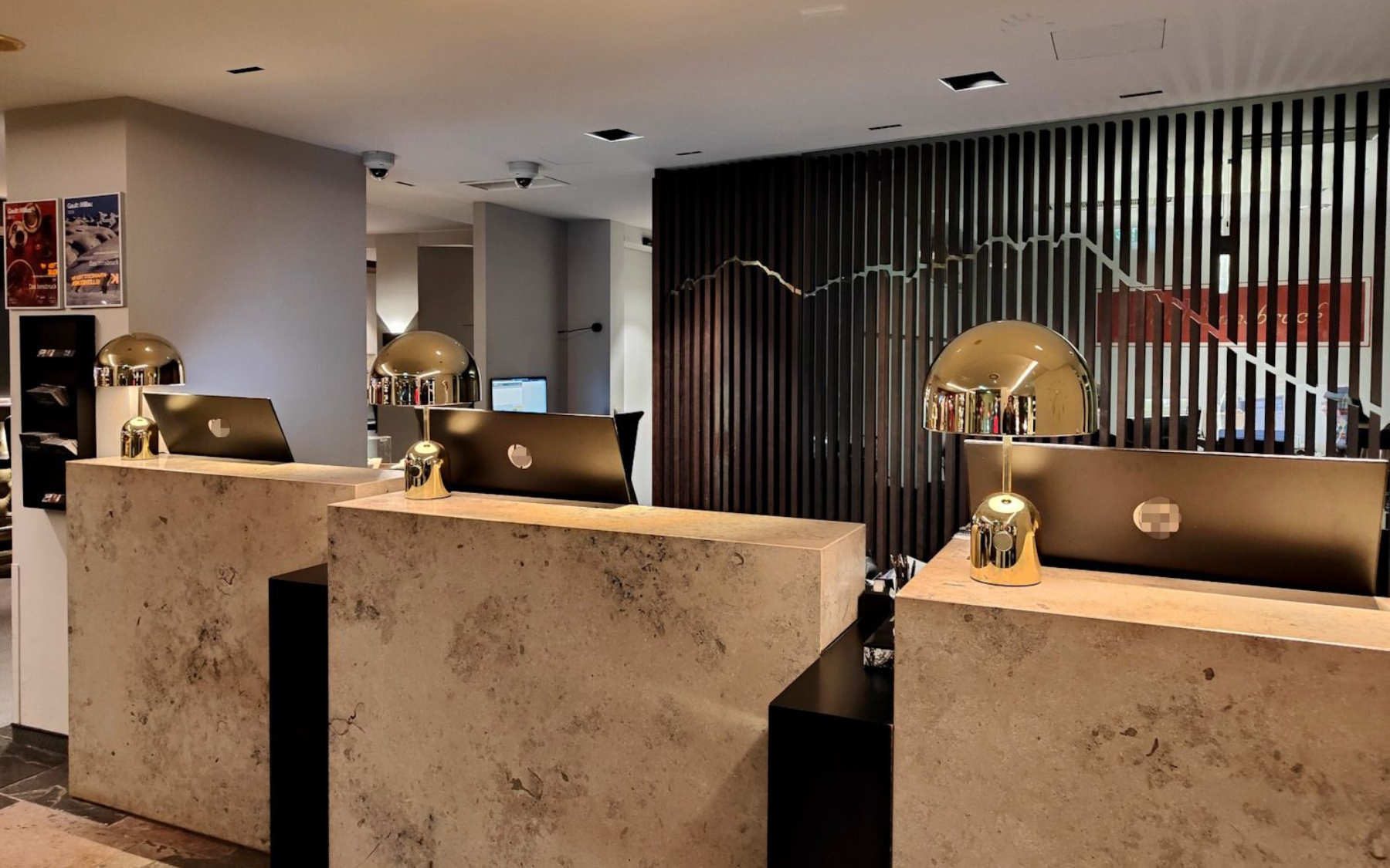 Hotel reception area with three stone-like counters. Dark wood panel backdrop, gold accents, and warm lighting.