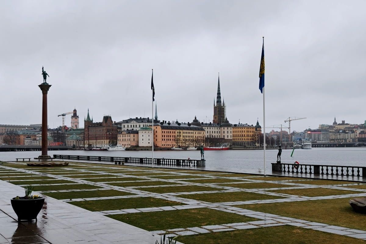 Snowy waterfront park with a city skyline and Swedish flags across the water