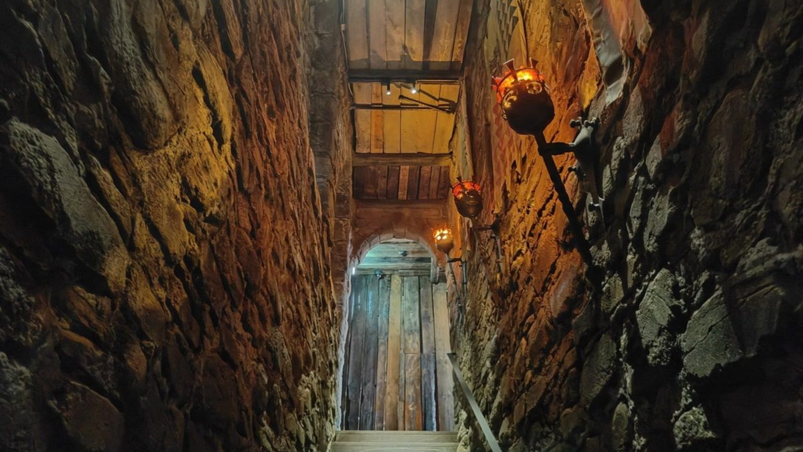 Deutschland Museum Berlin Stone corridor, dimly lit by sconces. A wooden door is visible at the end of the stairs.