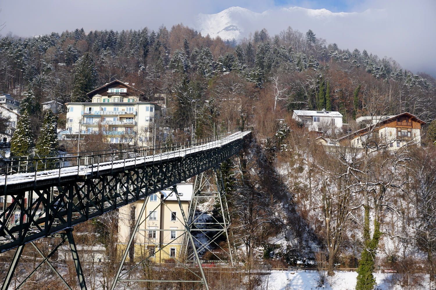 Snowy landscape with a bridge, buildings, and a mountain backdrop.