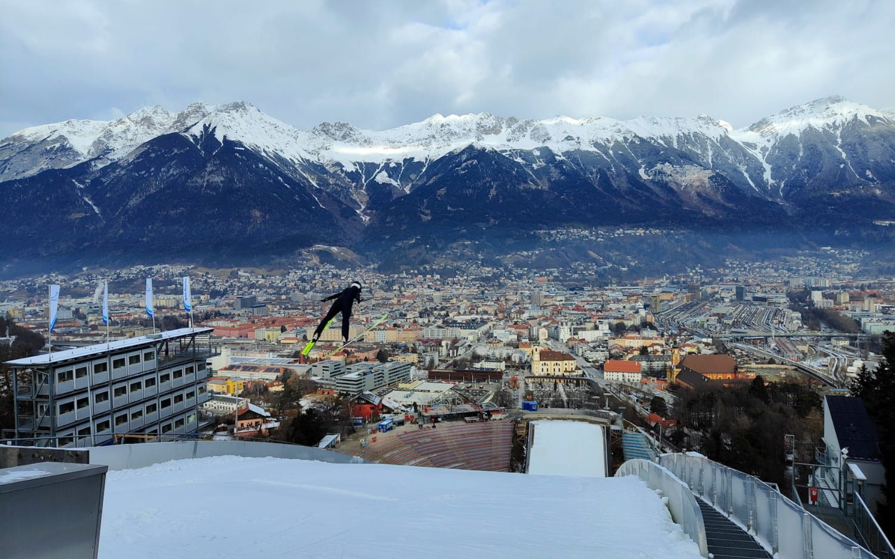 Ski jumper in mid-air above Innsbruck, Austria, with snowy mountains in the background.