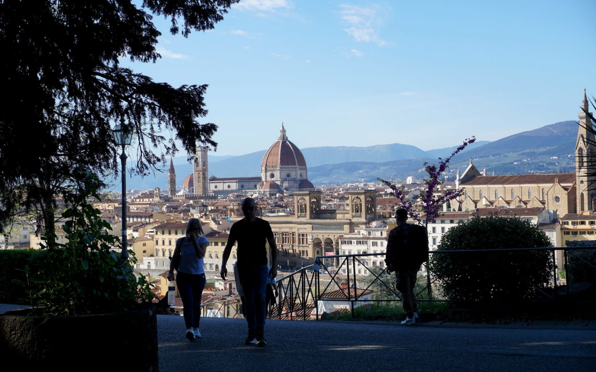People walking on a path overlooking the Florence Cathedral and cityscape on a sunny day.