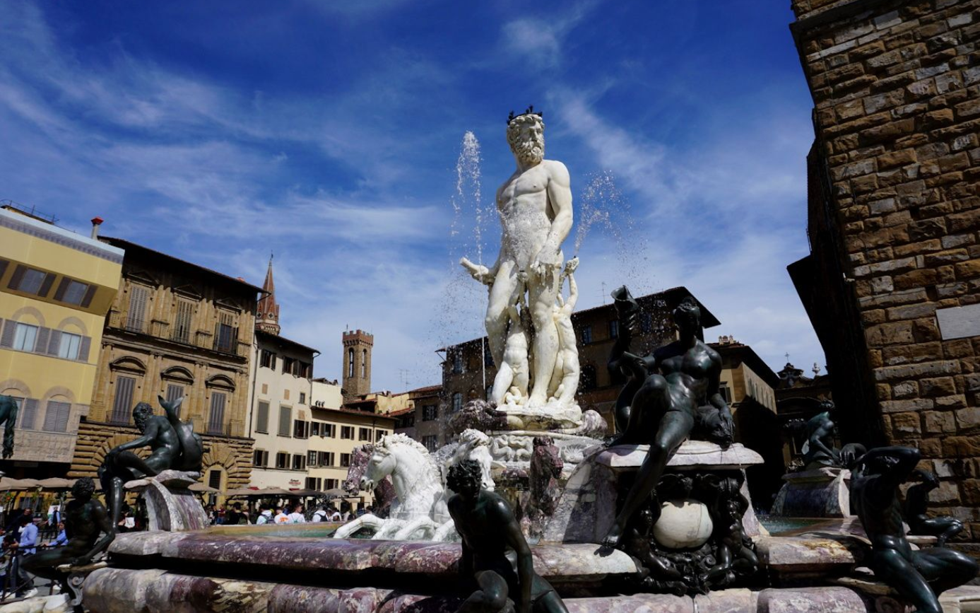 The Neptune Fountain with its central white statue surrounded by bronze figures in Florence's Piazza della Signoria.
