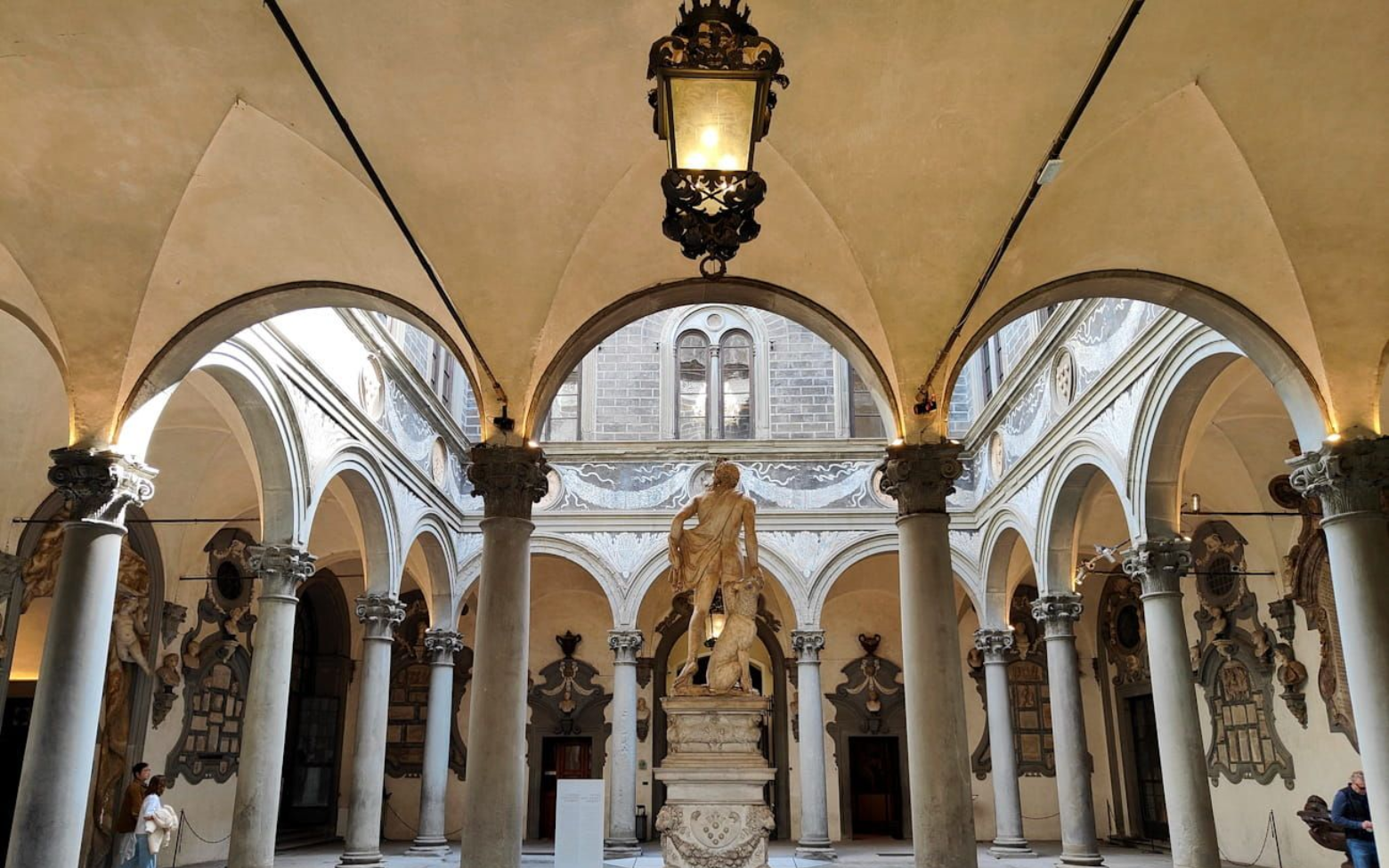 Ornate courtyard with a central statue, stone arches, and decorative columns in a historical building.