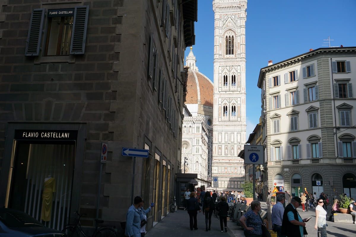 A street-level view of a narrow Florentine street leading toward the bell tower and dome of the Cathedral of Florence.
