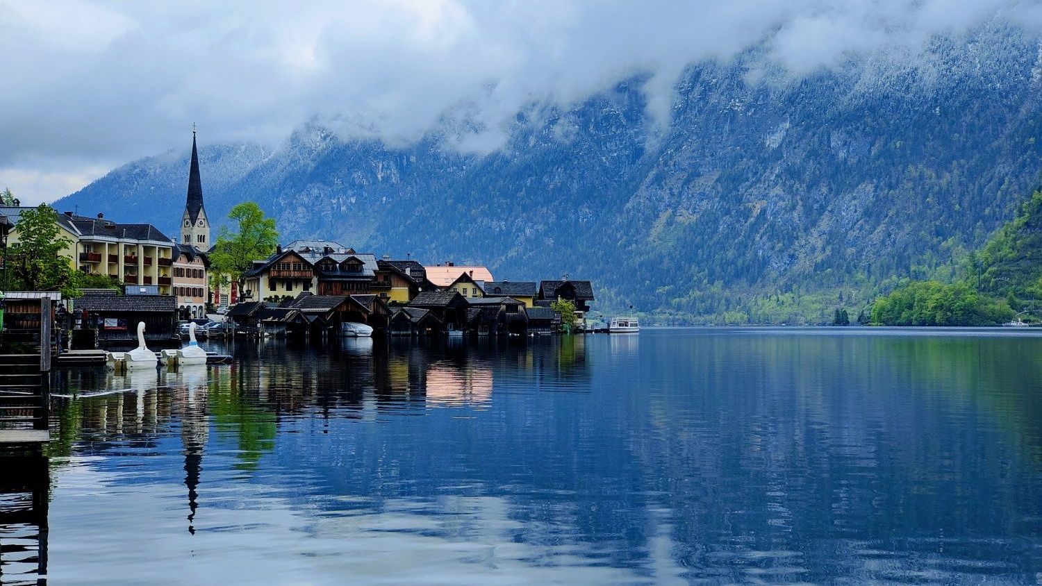 A small town sits on the shore of a lake with mountains in the background