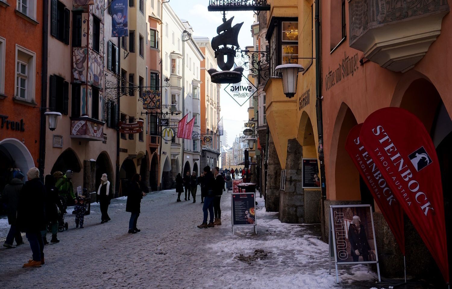 Snowy street in Innsbruck, Austria, with pedestrians and colorful buildings.