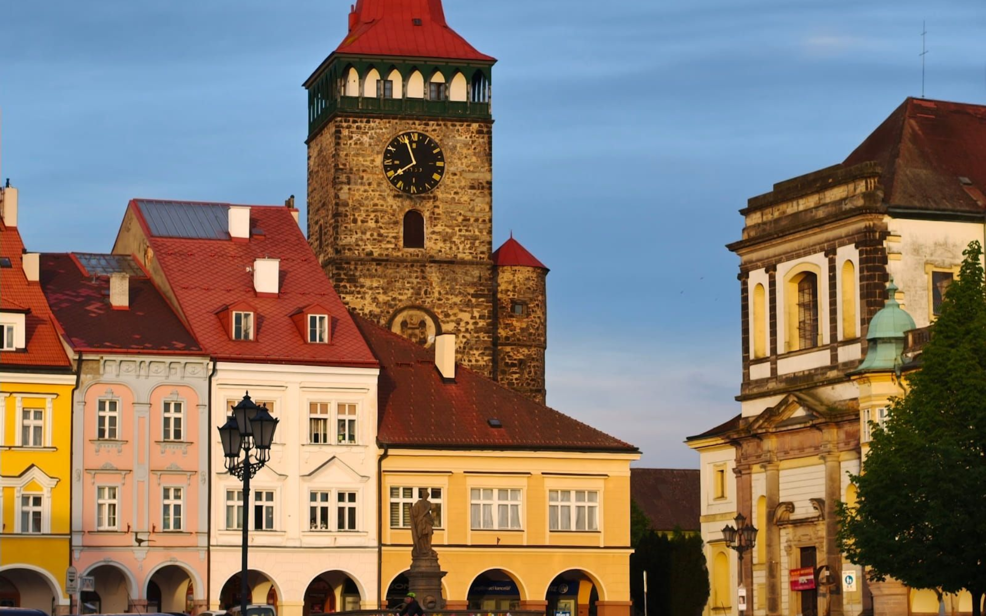 Colorful historic buildings and a stone clock tower under a blue sky in a European town square