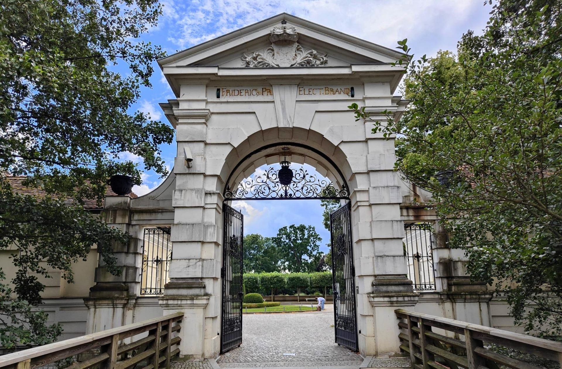 Köpenick Berlin Stone archway with open iron gates, leading to a garden; wooden bridge in the foreground.