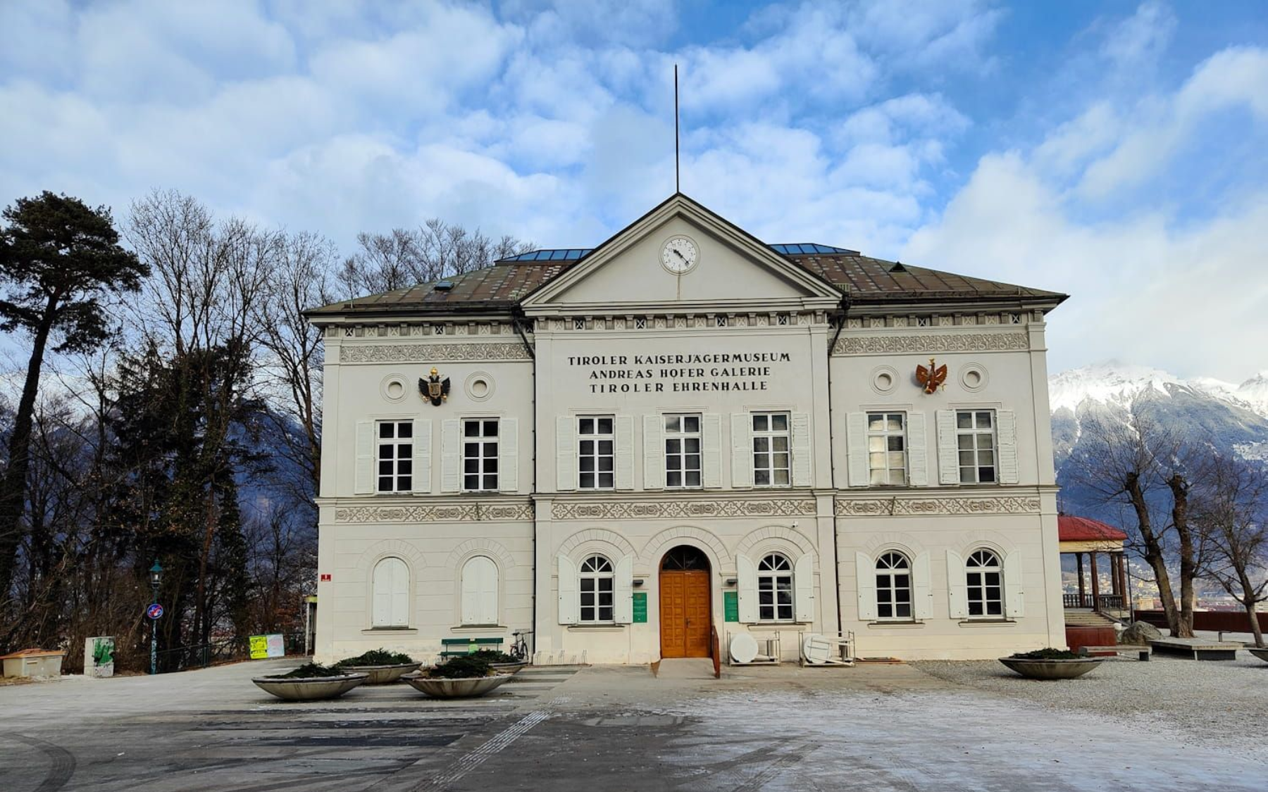 White building with clock, flag, and archway in a snowy outdoor setting.