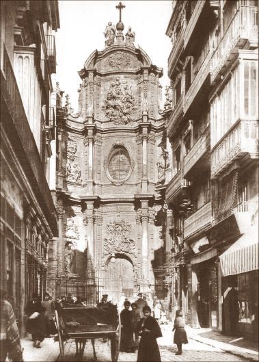 Gothic church facade at the end of a narrow street. People and a horse-drawn cart are in the street.