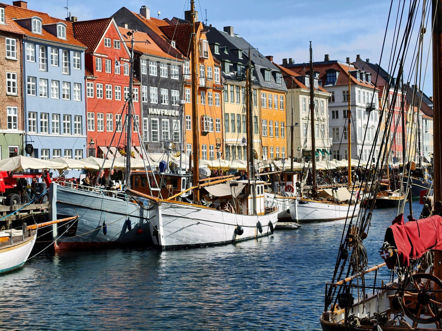 Colorful waterfront buildings and sailboats docked in a lively harbor on a sunny day