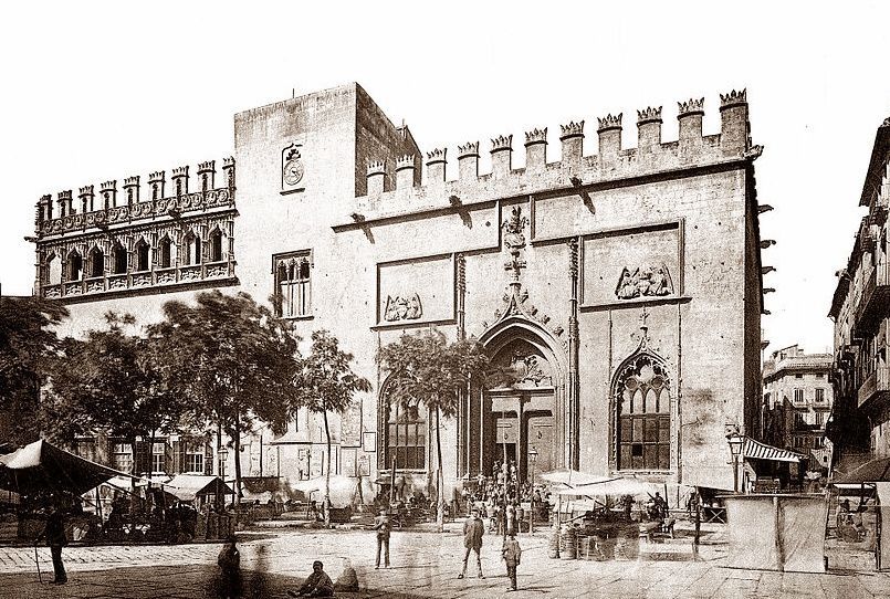 Historic stone building with crenellated roof and ornate facade, trees in foreground.