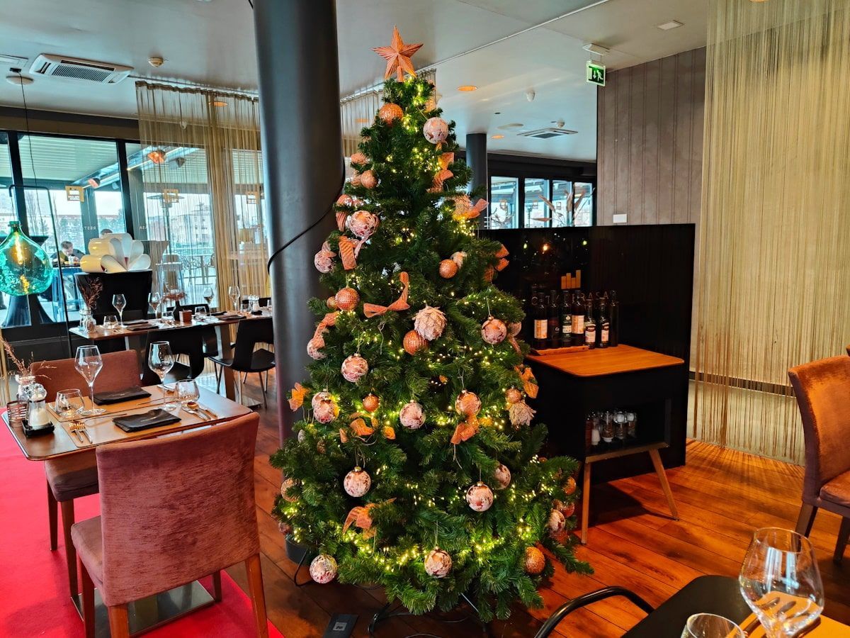 A Christmas tree decorated with ornaments inside a restaurant, tables set for dining.