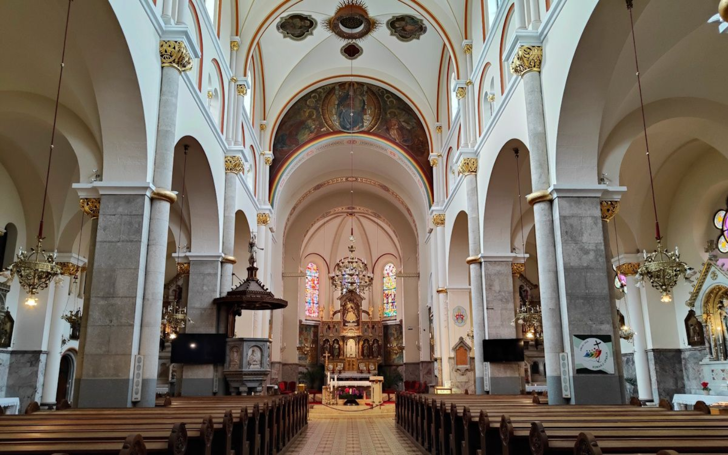 Maribor Kirche Interior view of a church with arched ceiling, columns, and rows of wooden pews. The altar is at the end.