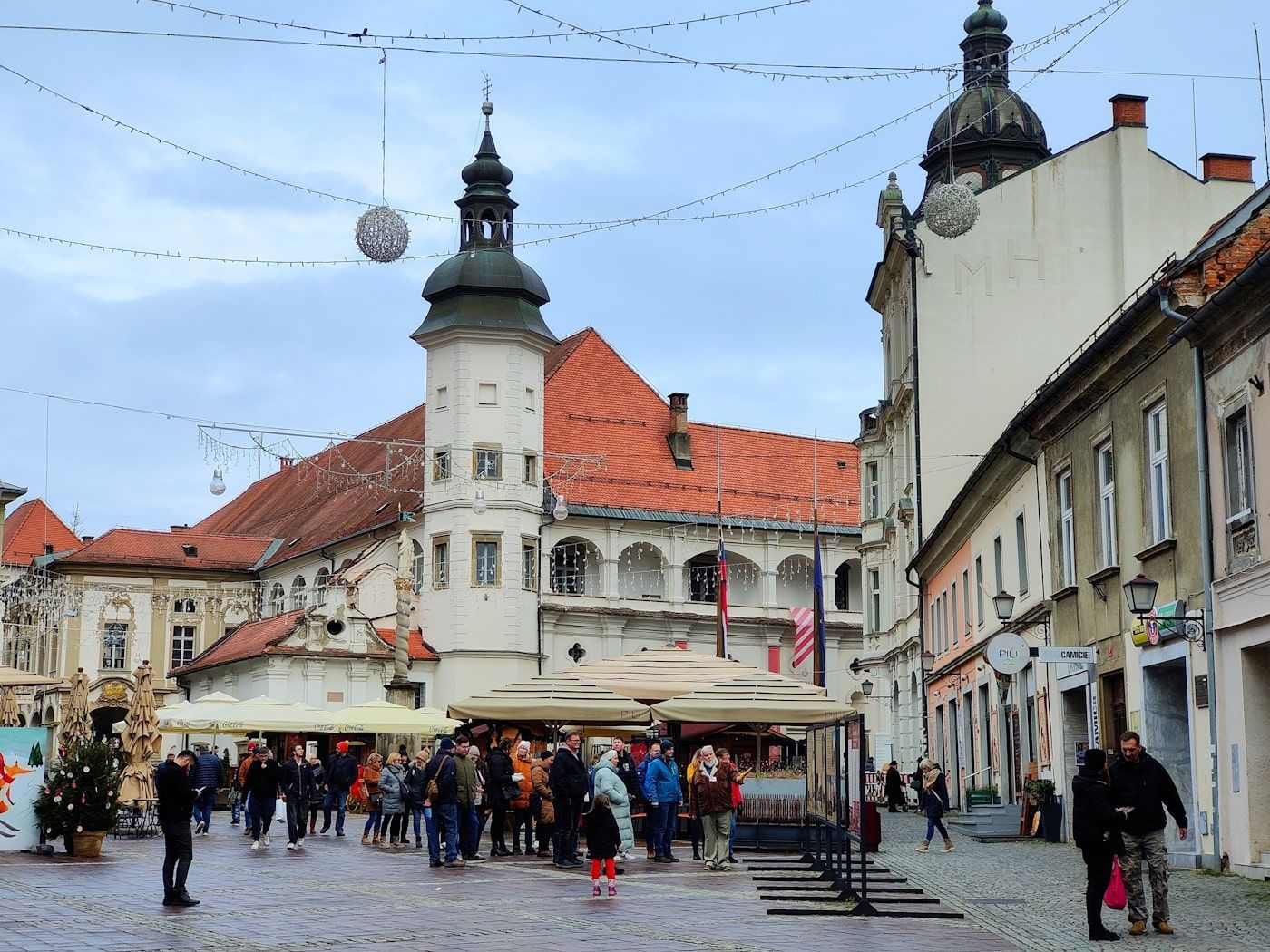 Maribor Schlossplatz Town square with people, historic buildings, and Christmas decorations under an overcast sky.