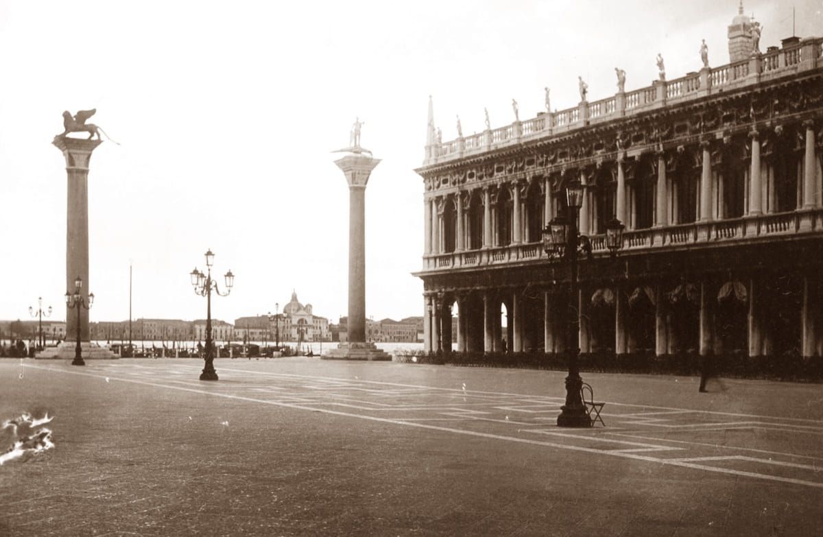 A sepia-toned view of St. Mark’s Square in Venice featuring the two columns and the Biblioteca Marciana building.