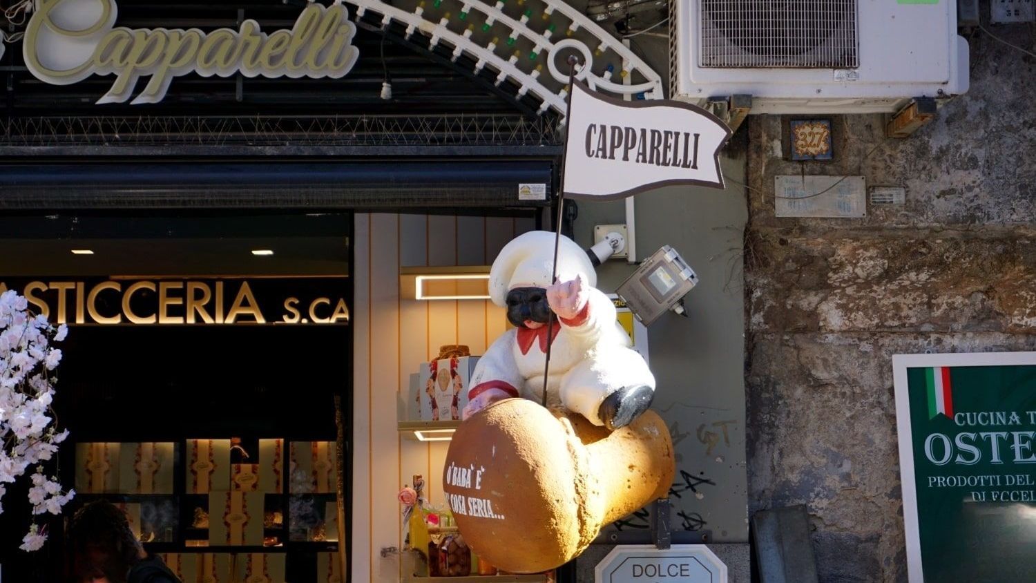 A stuffed animal is sitting on an ice cream cone in front of a store called capparelli